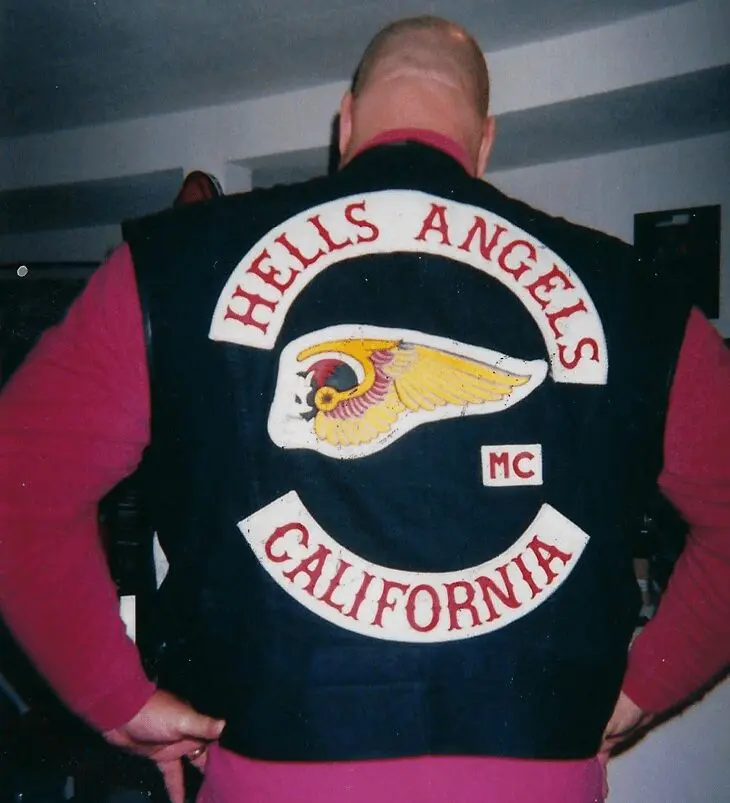 A man in a red shirt and black jacket with a hells angels mc patch on his back.